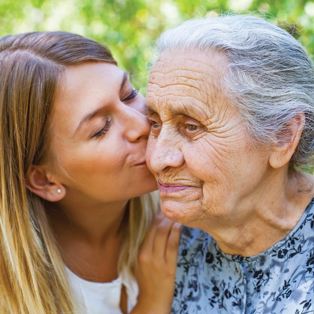 Granddaughter giving her elderly mother a kiss on the cheek.